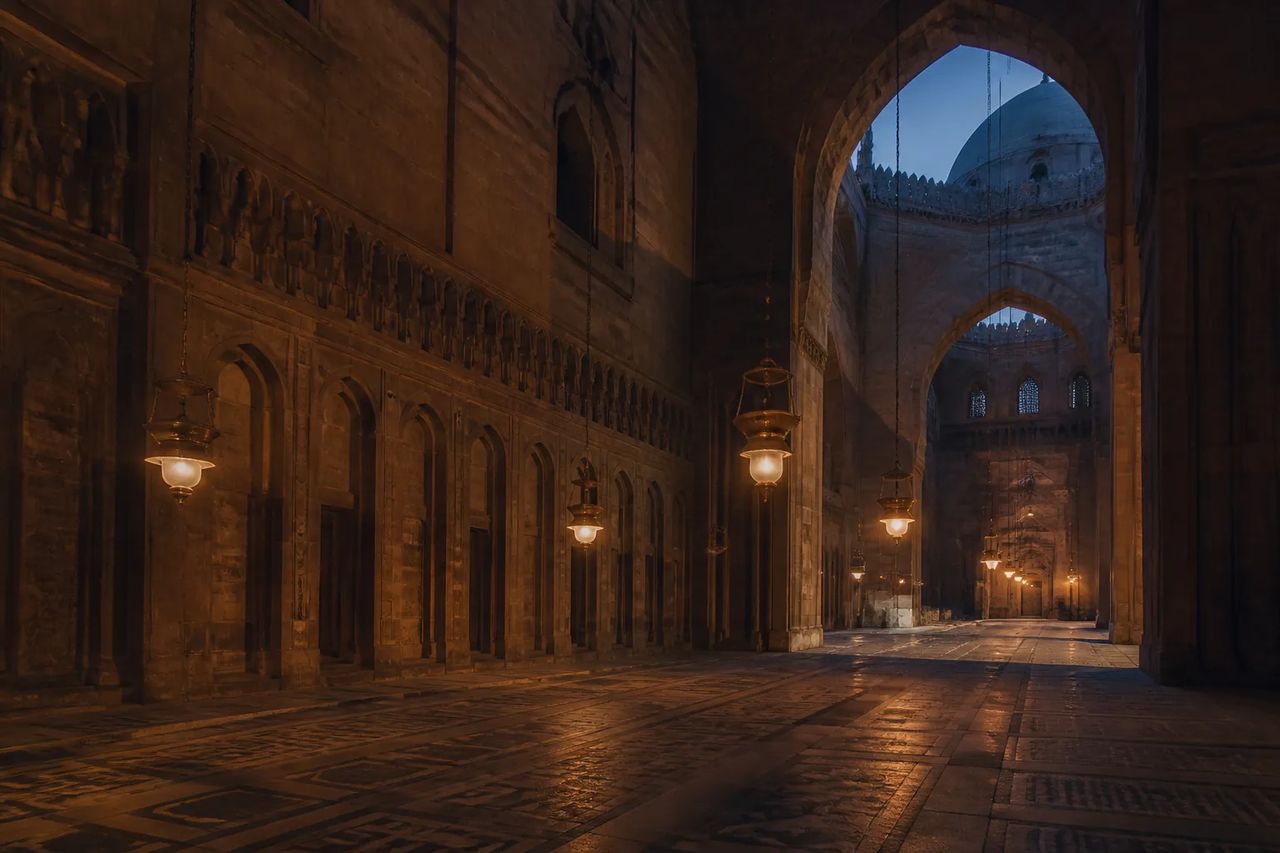 Interior of the Sultan Hassan Mosque in Cairo at dusk, sandstone iwans and mosque lamps