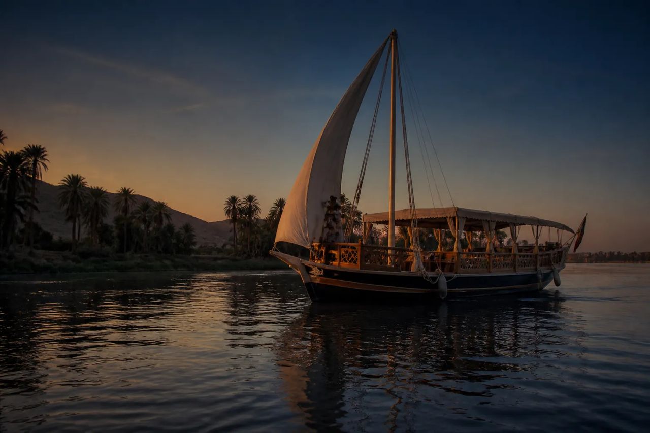 Traditional Dahabiya sailboat on the Nile, west bank palm groves behind
