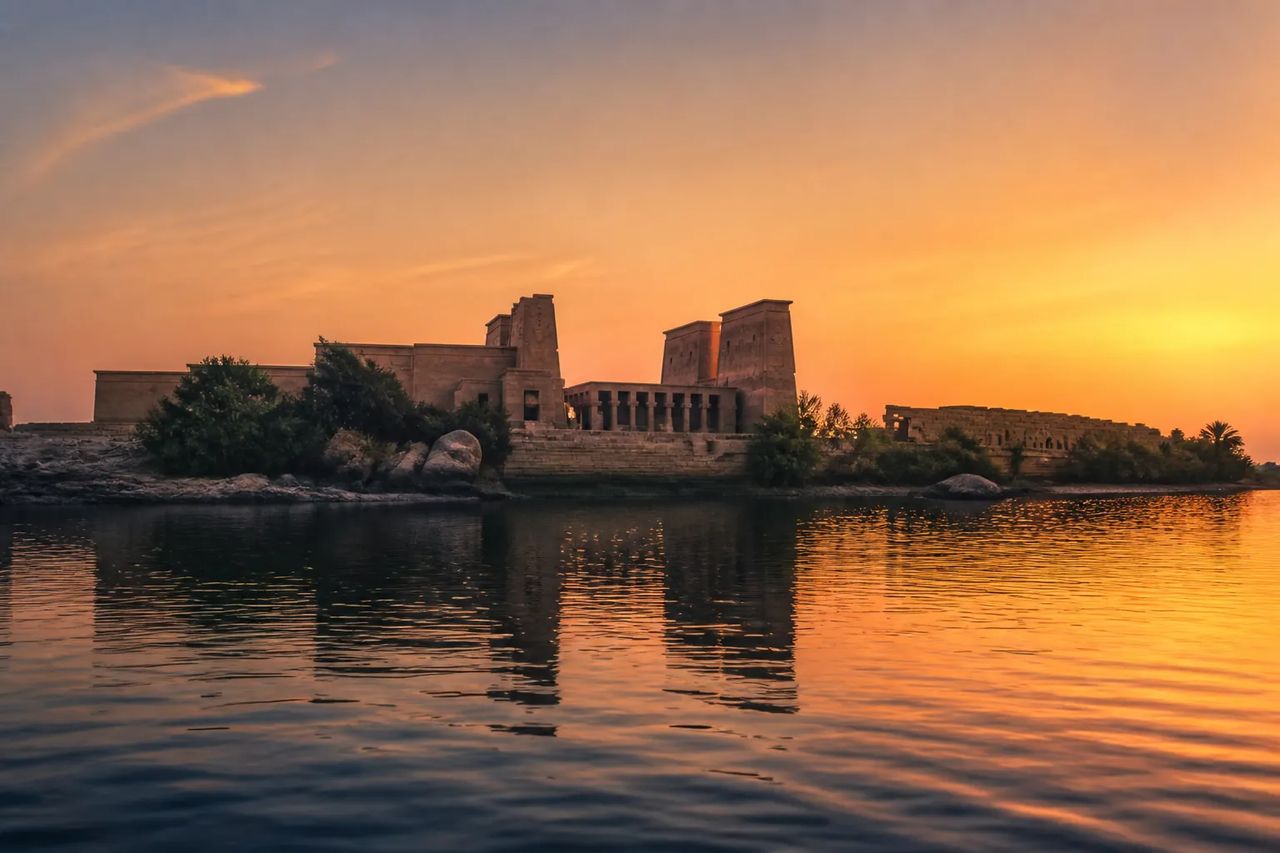 Philae temple complex on Agilkia Island at sunset, silhouetted against an apricot sky