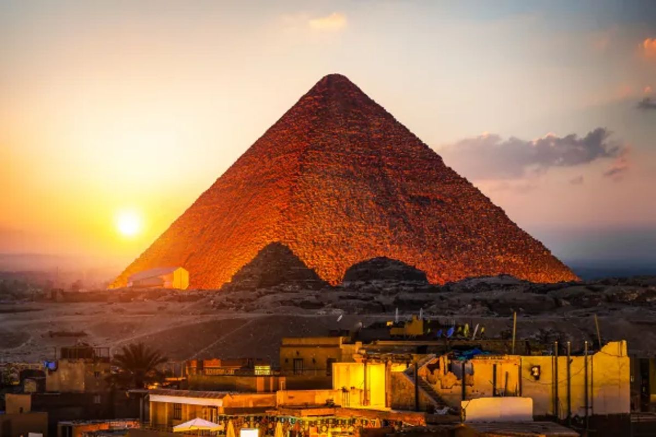 Pyramid at Giza lit by the setting sun above the houses of the plateau edge