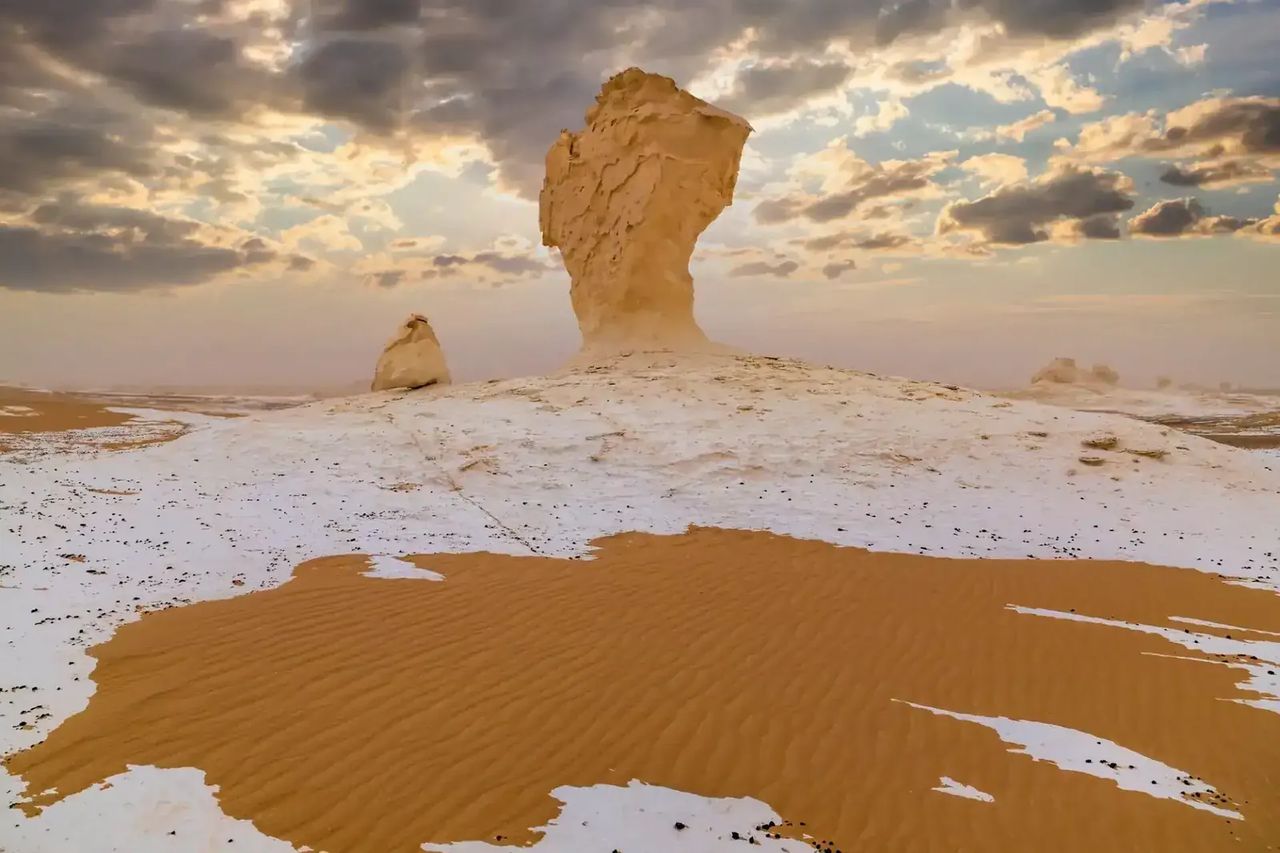 White chalk rock formation rising from sand and pale chalk crust under a cloudy sunset sky