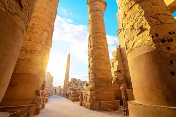 Sunlit columns of Karnak temple with an obelisk beyond