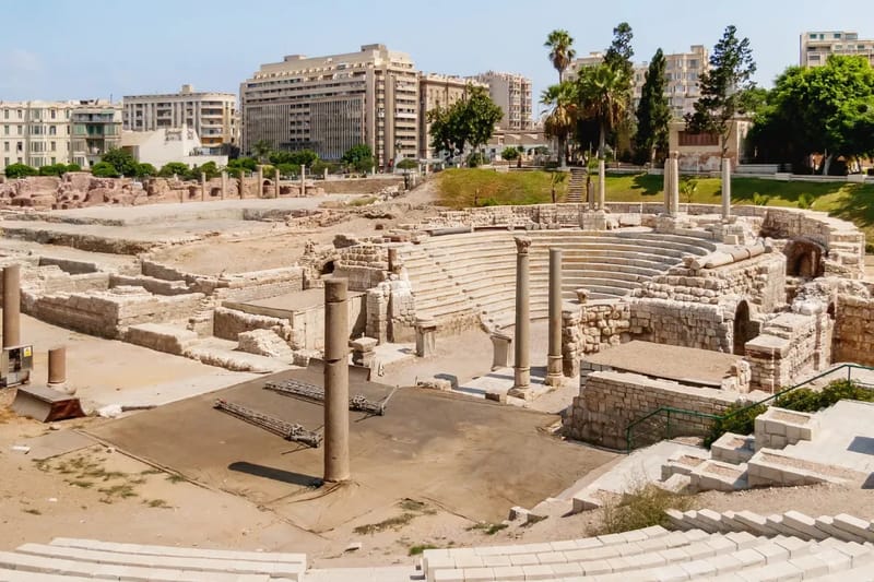 Excavated Roman theatre with tiers of seating and city buildings behind, Alexandria