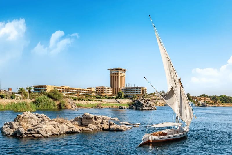 Felucca sailing on the Nile at Aswan past rocky islets and a hotel on the bank