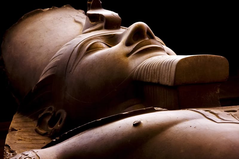 Face of the fallen limestone colossus of Ramesses II at Memphis, lit against a dark background