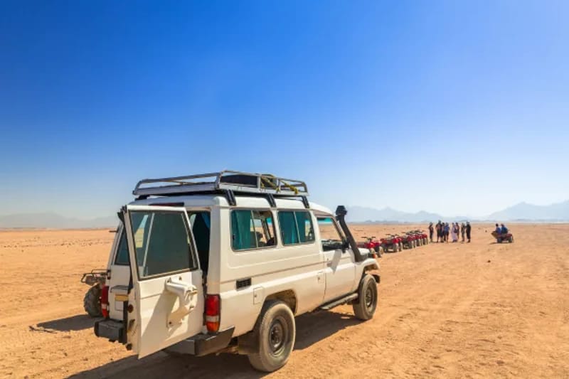 White safari jeep in open desert with a line of quad bikes behind