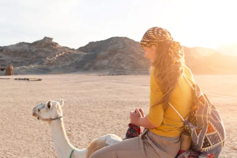 Woman in a yellow top riding a camel through sunlit desert hills