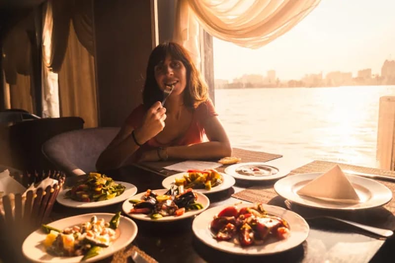Woman dining at a window table set with several plates of food, city skyline behind