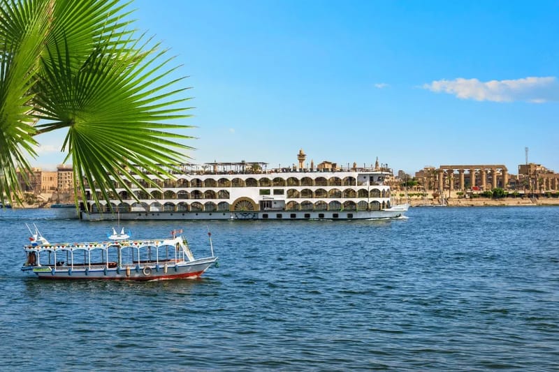 Nile cruise ship and a small boat passing Luxor temple
