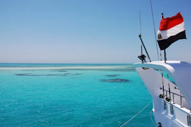 Bow of a white boat flying the Egyptian flag over turquoise water