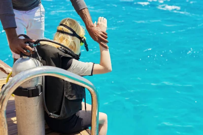 Diver being helped into scuba gear on the back of a boat