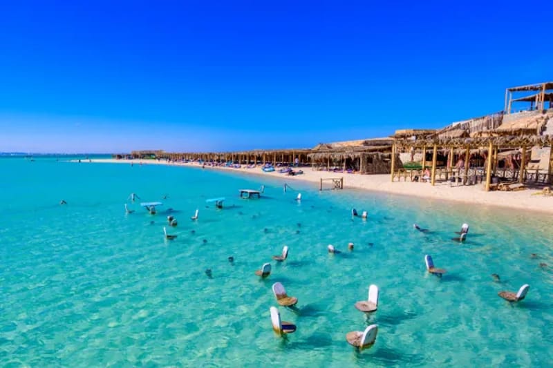 Shallow turquoise water and a beach with huts at Orange Bay